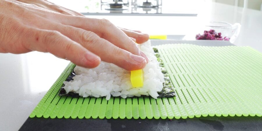 Placing a stick of takuan pickle on a sushi roll.