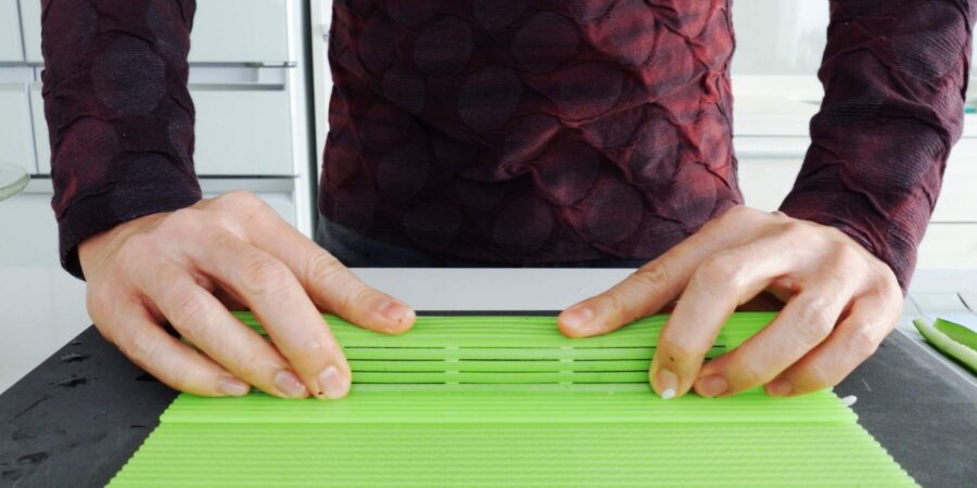 Pressing a sushi roll into shape using a sushi mat.