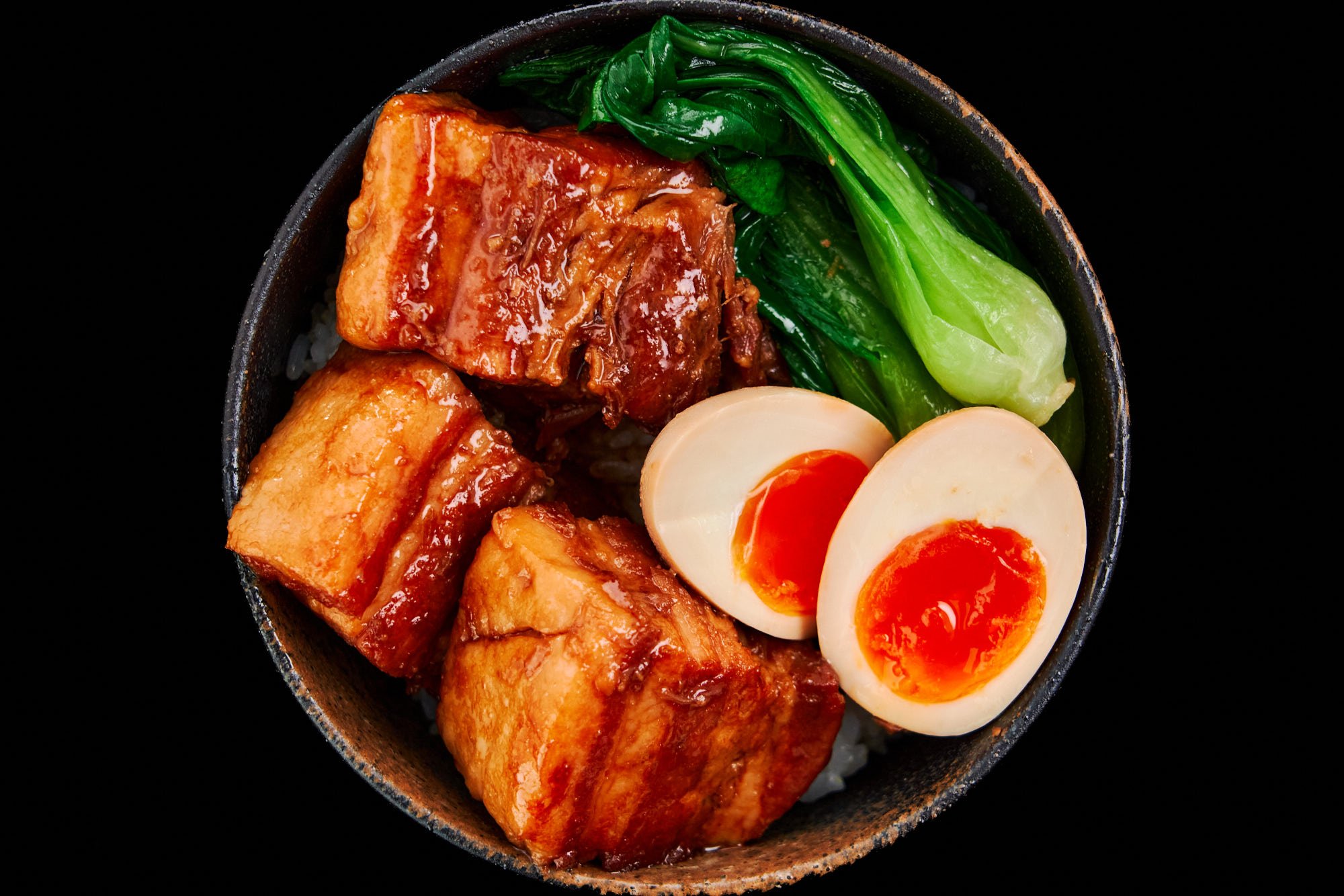 A hearty kakuni-don, featuring melt-in-your-mouth pork belly draped in its thickened braising sauce over steaming rice, topped with marinated eggs and crisp bok choy.