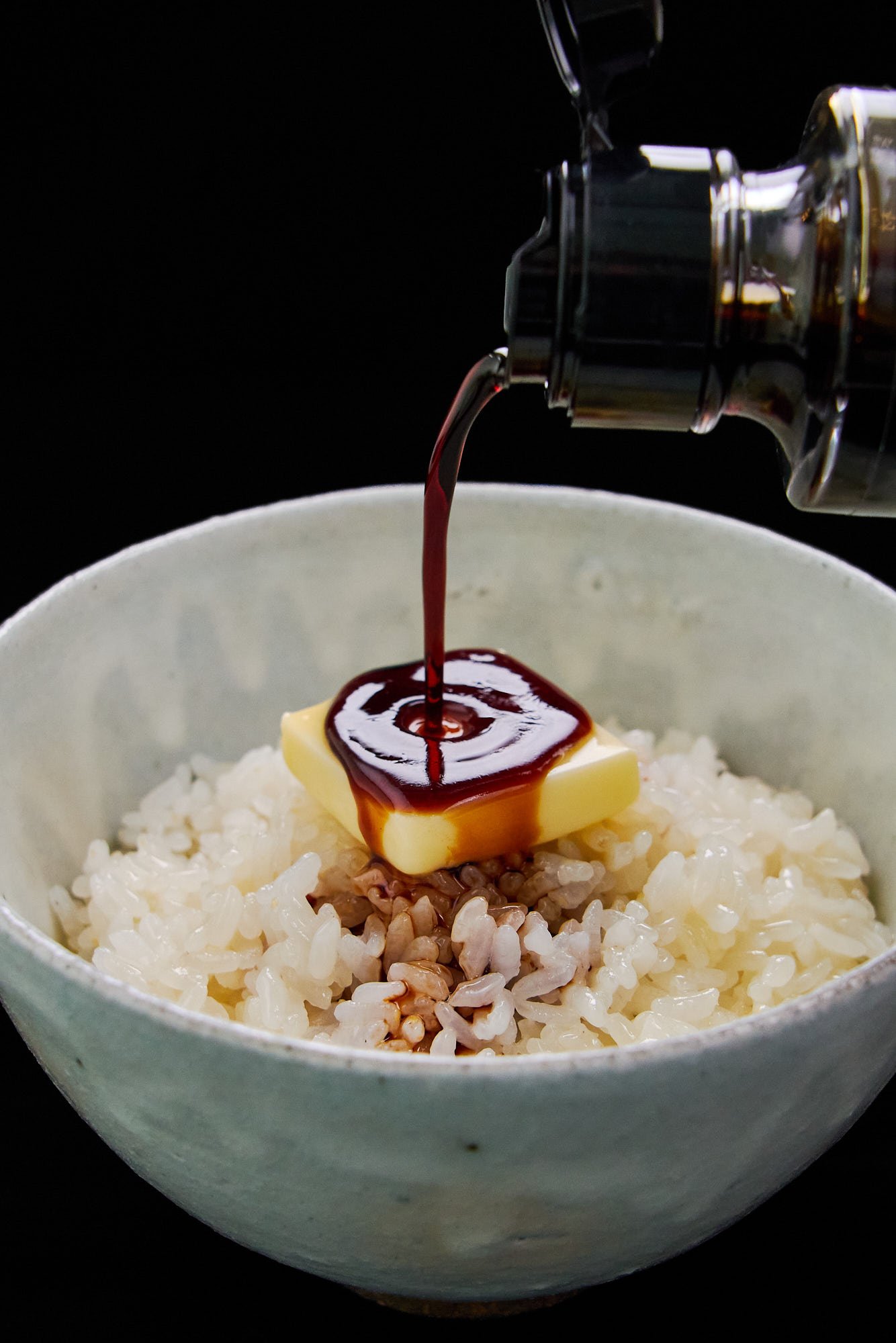 A savory drizzle of soy sauce pouring onto melting butter and hot rice, creating the ultimate bowl of comforting Japanese butter rice.
