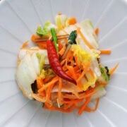Colorful mound of asazuke on a plate. Crisp napa cabbage, sallions, and carrots glisten with a red chili adding a bold accent.