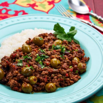 Close-up of Cuban picadillo on a turquoise plate showing the rich sauce with visible green olives, raisins, and ground beef garnished with fresh cilantro leaves.