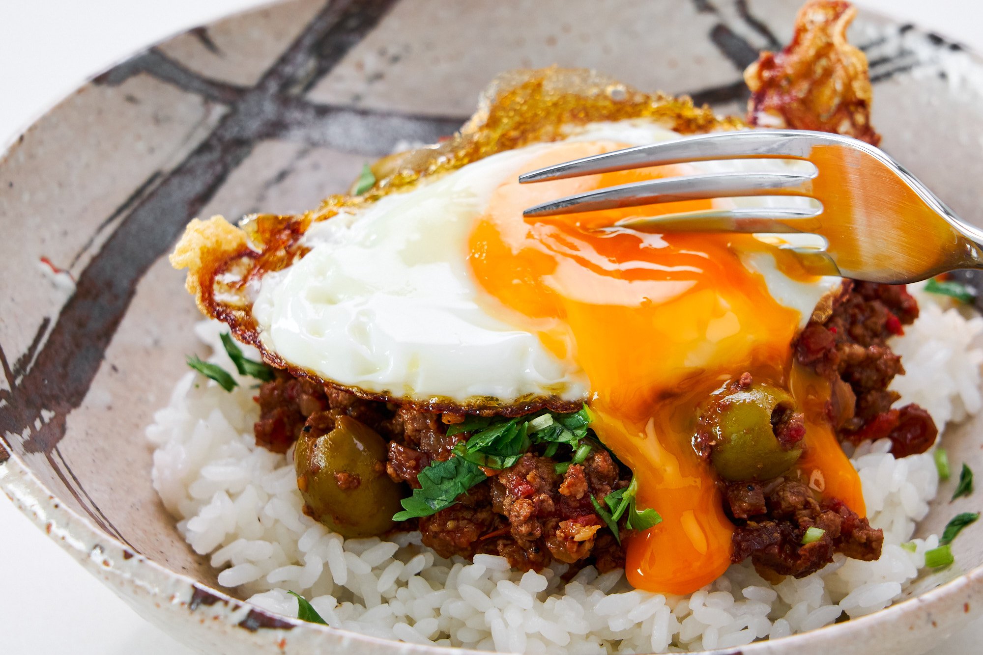 Cuban picadillo served over white rice topped with a cripsy fried egg, the runny golden yolk ready to mix into the savory beef, creating a rich sauce.